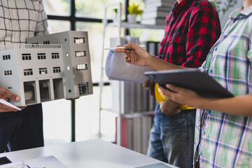Architects and engineers are having a meeting analyzing blueprints and a building model, discussing ideas and planning the next steps of the project.
