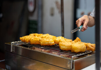 Close-up view of a street food cook turning freshly fried patongo dough with metal tongs, capturing the hot oil, golden texture, and authentic Thai street cuisine atmosphere.