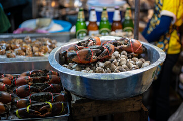 Live crabs stacked on a tray at a Thai street food stall, their claws tied as they wait for sale, capturing the raw and authentic atmosphere of local market life.