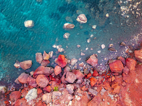 Aerial view of the striking contrast between the red rock formations and the turquoise waters of the Aegean Sea, Santorini, Greece.