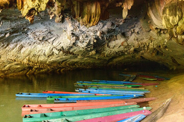 A row of brightly painted wooden boats floats on still water beneath dramatic limestone formations...