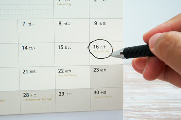Hand holding a pen circling Teacher’s Day on a monthly calendar, symbolizing appreciation for...