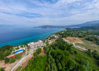 Fototapeta premium Aerial drone view of the scenic Lake Ohrid waterfront in North Macedonia, featuring red-roofed buildings, lakeside hotels, and the clear blue waters of this UNESCO World Heritage site.