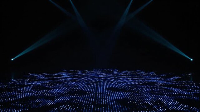 Dimly lit stage with blue grid floor, beams of light, fog, and a live concert performance.