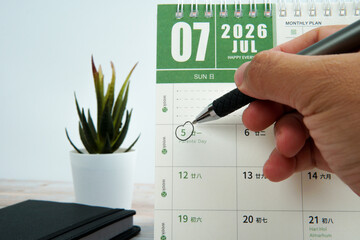 Close up hand holding pen marking Parents’ Day on calendar beside workspace desk. Concept of family appreciation, love, gratitude, annual reminder, and time management.