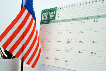 Wide shot calendar marking Malaysia Day with Malaysian flag beside desk. Concept of national pride,...