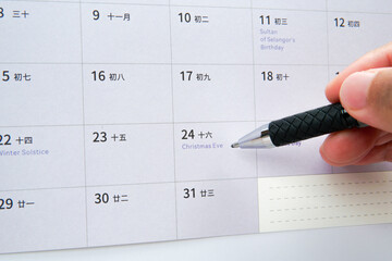 Close up hand holding pen pointing at Christmas Eve on calendar. Concept of festive season, year end celebration, holiday reminder, time management, and annual planning.