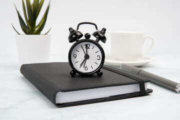 Business workspace with alarm clock on notebook, pen, coffee cup, and plant. Concept of time...