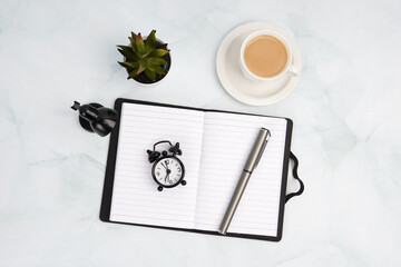Top view flat lay of open notebook with alarm clock, pen, coffee cup, plant, and desk lamp. Concept...