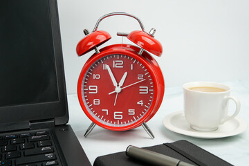 Office workspace with red alarm clock beside laptop, notebook, pen, and coffee cup. Concept of time...