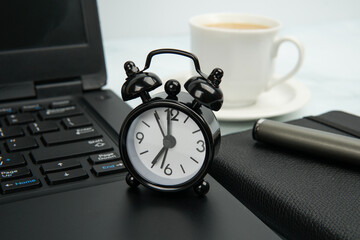 Office workspace with black alarm clock on laptop beside notebook, pen, and coffee cup. Concept of...