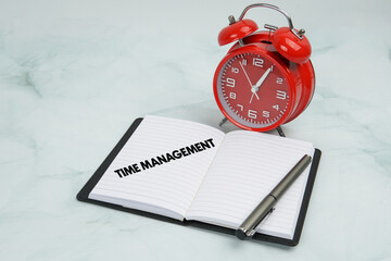 Open notebook with “Time Management” text, pen, and red alarm clock on marble background....