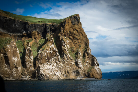 View of a dramatic cliff face plunges into the sea, its rugged textures and contrasting colors painting a vivid scene of nature's raw power, Saudarkrokur, Drangey Island, Iceland.
