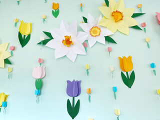 Colorful flower garlands and large paper blooms adorn a kindergarten wall, creating a cheerful and vibrant atmosphere for children's learning and playtime activities with copy space