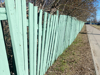 Colorful wooden fence painted in mint green stands along a grassy pathway, creating a vibrant boundary between nature and urban environment, enhancing outdoor aesthetics