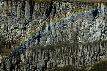 View of a vibrant rainbow arched across a rugged, rocky cliff face in Dettifoss waterfall, Vatnajokull Park, Northeast Iceland, Iceland.