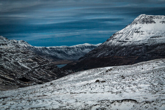 View of snow-covered mountains under a cloudy sky create a stark contrast, evoking a sense of serene desolation in Seydisfjordur, East Fjords, Iceland.