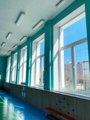Bright and airy interior of a sports hall featuring large windows, turquoise walls, and natural light illuminating the polished floor, creating an inviting atmosphere for physical activities