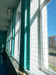 Interior of a school gym with large windows allowing natural light, showcasing vibrant turquoise walls and a spacious atmosphere for sport education and activities with copy space