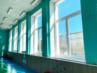 Bright interior of a school gym with large windows, showcasing vibrant blue flooring and natural light, creating an inviting atmosphere for sport education activities