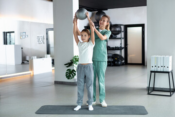 Little girl standing arms outstretched on stability ball female therapist