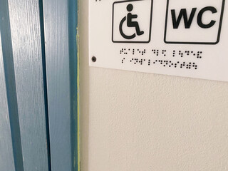 Accessible restroom sign featuring Braille and wheelchair symbol, mounted on a wall, indicating facilities for individuals with disabilities, promoting inclusivity and accessibility