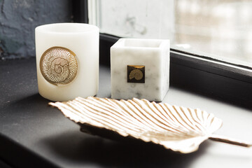 Elegant candles in decorative holders placed on a windowsill, accompanied by a stylish leaf-shaped dish, creating a serene and inviting atmosphere for home decor enthusiasts