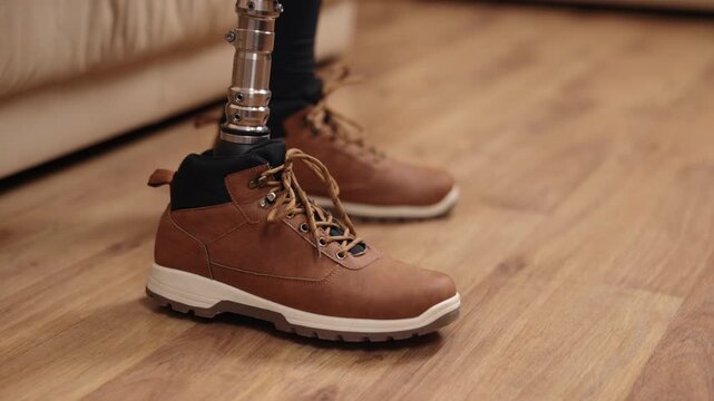 mobility aid, independent living, close-up shot. Man with prosthetic leg captured up close putting on shoes on sofa, crutches lying beside him.