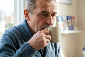 Elderly man drinking coffee with sad expression