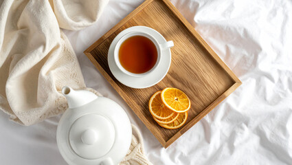 tea in bed with white teapot, wooden tray, and dried orange slices on white linen