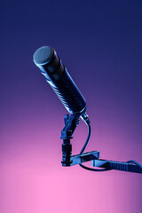 A black microphone is mounted on a stand, positioned in front of a vibrant, colorful background. This setup is typical in a recording studio or performance space focused on sound.