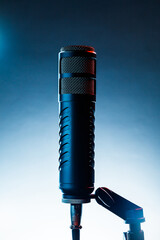 A vintage microphone is positioned on a stand with a soft blue background. The setup suggests a space for music or podcast recordings. The microphone is shining with vivid details.