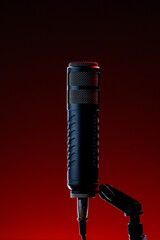 A microphone stands on a mount with a red background. The scene shows a recording area prepared for audio work. The lighting highlights the microphone's design.