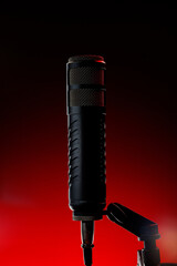 A black microphone is placed on a stand with a red background. The scene shows a music recording setup, highlighting the microphone as the focus during the session at night.