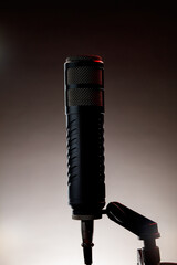 A black microphone stands upright on a mount. Soft lighting creates a shadowy background. This setup is typical in a recording studio setting during the evening hours.