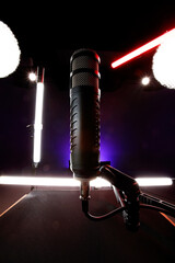 A microphone stands in front of bright studio lights. The setup creates a focused environment for recording. Cables connect the microphone to other equipment behind it.