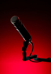 A microphone is mounted on a stand with a black finish, positioned in front of a bright red background. The setup is for a recording session in a studio.