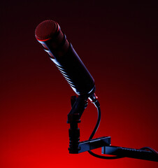 A studio microphone is positioned on a stand with a sturdy clamp. The background is dark with red lighting. The setup suggests a recording session for audio or music.