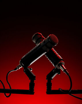 Two black microphones are positioned on a stand with a red background. The microphones are angled towards each other, suggesting a conversation or performance setting.