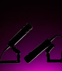 Two distinct microphones are positioned opposite one another in a low light space. A purple backdrop enhances the focus on the equipment.