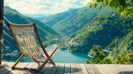Tranquil wooden deck with comfortable lounge chair overlooks breathtaking vista of serene blue lake nestled amidst verdant, rolling mountains, under clear, sunny sky, inviting relaxation and escape.