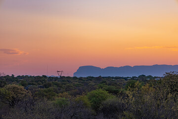 Orange and purple sunset sky over silhouetted mountains and green bushland. Natural evening landscape for travel and vacation concepts.