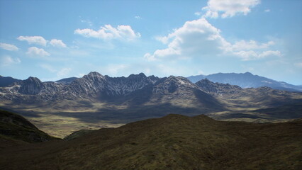 Expansive rocky mountain range under sky with scattered clouds, golden grassy foreground, jagged ridgelines and distant plateaus, crisp light creating dramatic