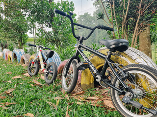 Obraz premium Depok - Indonesia, Dec 12, 2025: Two bicycles resting by a colorful tire barrier in a lush green outdoor park setting, symbolizing play and recreation