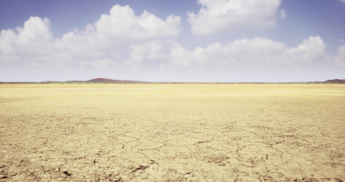 A dry landscape with cracked earth extends infinitely under a bright blue sky filled with fluffy clouds. The scene conveys a sense of emptiness and natural beauty during daytime.