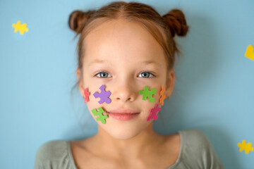 Portrait of a girl with pieces of multicolored puzzles pasted on her cheeks, a symbol of autism. Support and care for people with autism spectrum disorder. Education and social equality.