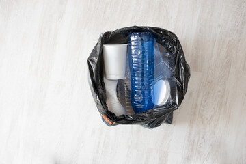 Plastic waste inside black garbage bag on light floor with copyspace, environmental protection, recycling