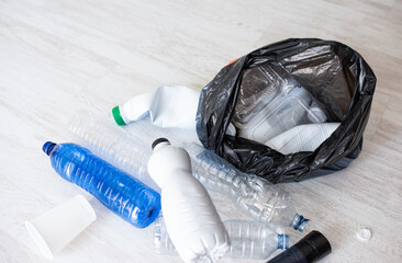 Scattered plastic bottles near black garbage bag on light floor, recycling business or eco campaign mockup
