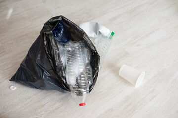 Plastic bottles falling out of black bag on bright floor, environmental cleanup, waste management or eco app
