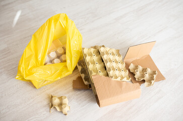 Yellow bag with paper egg cartons and cardboard on bright floor, recycling company or eco mockup with copyspace
